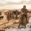 Moses strikes a large rock with his staff as water pours out before Israelites, livestock, and tents in the desert.
